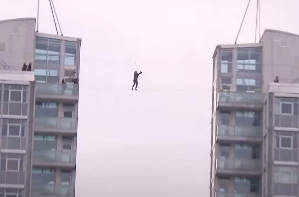 Person balanciert auf einer Slackline, die zwischen zwei Hochhäusern in schwindelerregender Höhe gespannt ist